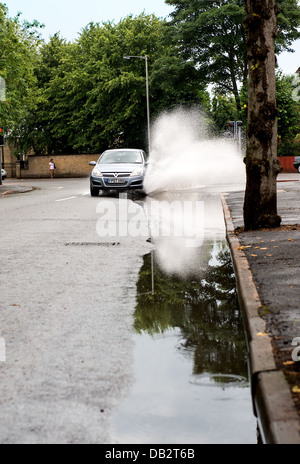 Une voiture roule dans une flaque d'eau après une période de pluies torrentielles. Banque D'Images