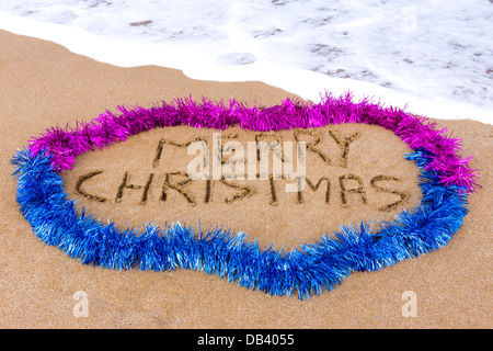 Joyeux Noël écrit dans le sable avec des guirlandes et mer en arrière-plan Banque D'Images