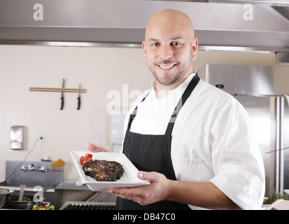 Young male chef présentant un juteux ribeye steak avec des tomates Banque D'Images