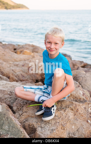 Portrait of young smiling blonde boy, siiting sur une pierre à la côte de la mer Noire Banque D'Images