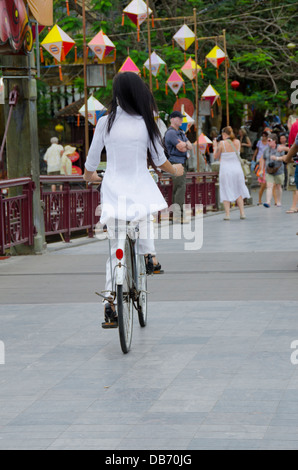 Vietnam, Da Nang. Hoi An. Hoi An une passerelle sur la rivière Thu Bon. Jeune fille en uniforme de l'école en vélo. Site de l'UNESCO. Banque D'Images