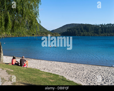 dh Lake Tikitapu Blue Lake ROTORUA NEW ZEALAND couple assis détente sur le rivage baigneurs vacances lagon lacs Banque D'Images
