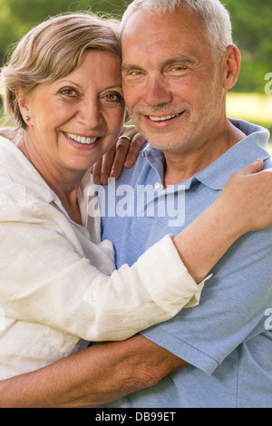 Senior couple hugging and smiling in park looking at camera Banque D'Images