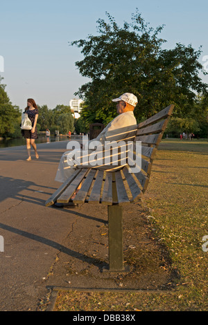 Homme assis sur un banc dans un parc, à observer une fille à pied par. Banque D'Images