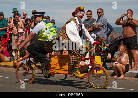 Swanage, Dorset, Royaume-Uni. 28th juillet 2013. Des milliers de visiteurs descendent sur Swanage pour assister à la procession, dans le cadre de la semaine du carnaval de Swanage. Clown et l'agent de soutien communautaire de la police font du bak pour bak sur le vélo de clown à l'amusement de la foule et des enfants. Crédit : Carolyn Jenkins/Alay Live News Banque D'Images