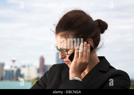 Jeune femme d'affaires en costume blouson écoutant sur un smartphone, travaillant avec le centre ville en arrière-plan Banque D'Images