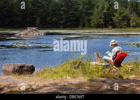 Une femme peint un lac et un beaver house au bord d'un lac, dans le parc national Acadia sur Mount Desert Island dans le Maine Banque D'Images