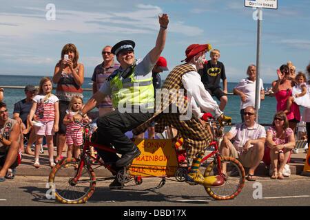 Swanage, Dorset Royaume-Uni 28 juillet 2013. Des milliers de visiteurs descendent sur Swanage pour assister à la procession, dans le cadre de la semaine du carnaval de Swanage. Clown et l'agent de soutien communautaire de la police font du bak pour bak sur le vélo de clown à l'amusement de la foule et des enfants. Crédit : Carolyn Jenkins/Alay Live News Banque D'Images