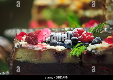 Tranche de cheesecake aux baies garnie de myrtilles, de framboises et de fleurs comestibles exposées dans un café. Banque D'Images