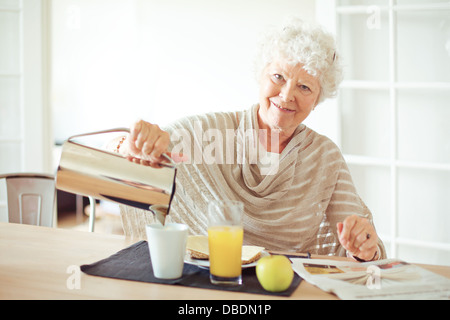 Happy senior femme qui a son petit déjeuner à la maison en vous regardant Banque D'Images