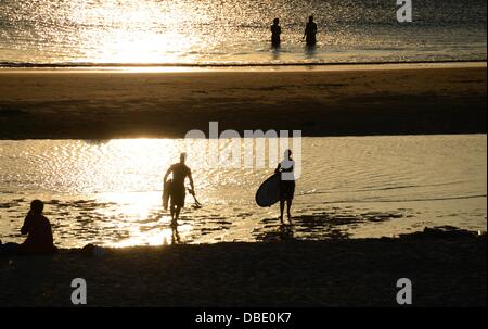 Surfers sortent de l'eau et marcher le long de la plage à la lumière du soleil couchant sur la plage de Westerland Sylt, Allemagne, le 23 juillet 2013. Photo : Jens Kalaene Banque D'Images
