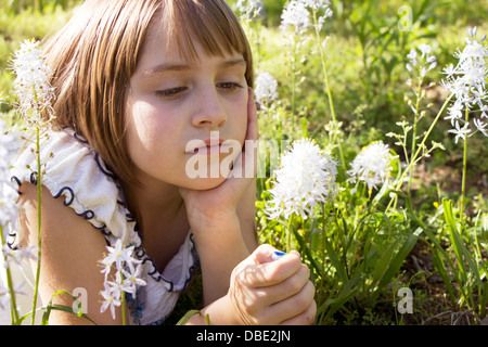 Jeune fille qui envisagent une fleur à l'extérieur. Banque D'Images