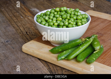 Des petits pois dans un bol dans cadre rustique avec des gousses de pois Banque D'Images