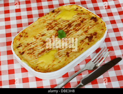 Poisson traditionnel fait maison tarte dans une casserole avec la purée de pommes de terre croustillante sur le dessus sur une nappe en vichy rouge Banque D'Images