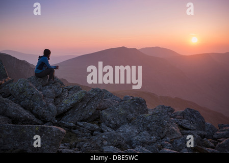 Female hiker watches coucher de soleil sur les montagnes depuis le sommet de Glyder Fach, parc national de Snowdonia, Pays de Galles Banque D'Images