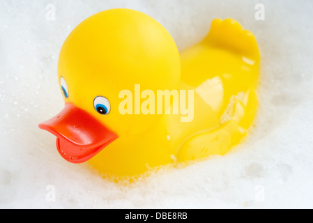 Un canard en caoutchouc jaune vif flottant dans les bulles blanches d'un bain à bulles. Banque D'Images