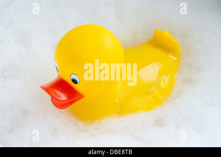 Un canard en caoutchouc jaune vif flottant dans les bulles blanches d'un bain à bulles. Banque D'Images