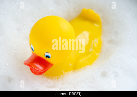 Un canard en caoutchouc jaune vif flottant dans les bulles blanches d'un bain à bulles. Banque D'Images