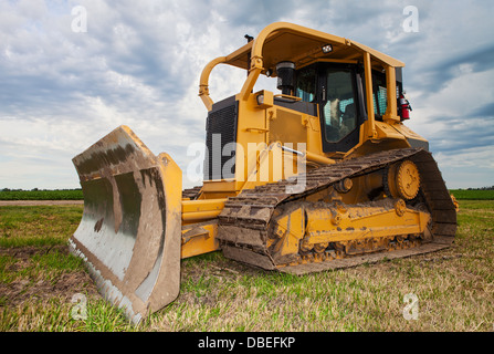Un grand bulldozer jaune sur un chantier de construction à proximité d'un champ d'agriculteurs Banque D'Images