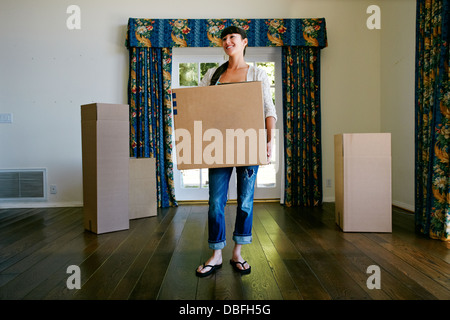 Mixed Race woman carrying box in new home Banque D'Images