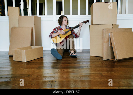 Young man playing guitar in new home Banque D'Images
