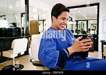 Hispanic woman using cell phone in salon Banque D'Images