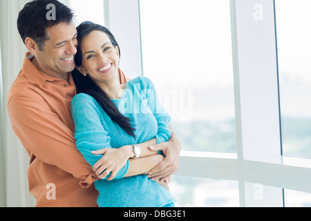 Hispanic couple hugging at window Banque D'Images