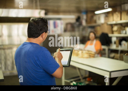 Hispanic baker using tablet computer in kitchen Banque D'Images