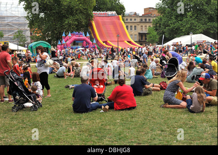 Des foules de gens en relaxant au soleil de Queen Square Bristol Park pendant Harbour Festival avec amusements gonflables en arrière-plan Banque D'Images