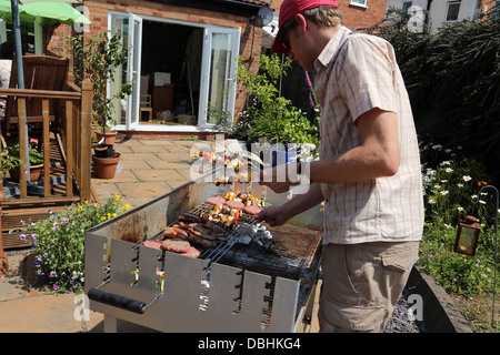 Man Cooking des hamburgers, des kebabs et des saucisses sur le barbecue dans le jardin en été Birmingham West Midlands England Banque D'Images