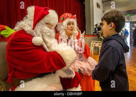 La sourde Hispanic boy communique avec un Père Noël sourd et Mme Santa en langue des signes lors de fêtes de Noël Banque D'Images