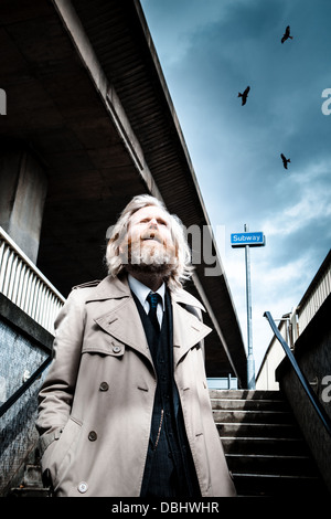 Homme barbu en costume et manteau walking down steps dans un métro, les oiseaux qui survolent la menaçante. Banque D'Images