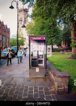 Une cabine téléphonique britannique Phone Booth - publiphone, vide en face de la cathédrale de York avec les piétons marcher passé. Banque D'Images