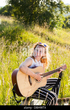 Adolescente qui joue de la guitare dans les champs. À l'extérieur. L'été. Banque D'Images