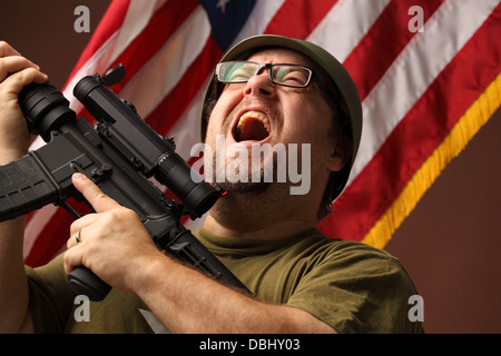 GI agressif dans t-shirt détient avec lunette de tir d'un fusil d'assaut et des hurlements pour ouvrir la bouche en face de stars and stripes Banque D'Images