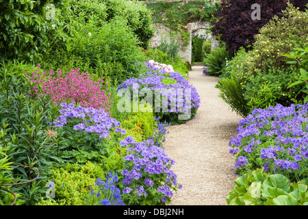 Ligne de frontières herbacées colorées un large chemin menant à une arche en pierre, le jardin clos, Rousham House, Oxfordshire, Angleterre Banque D'Images