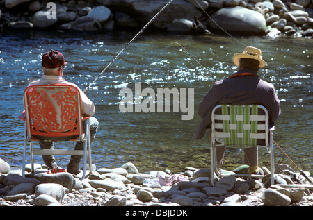 Deux pêcheurs à la retraite se relaxer sur leur chaise de jardin sur les rives du ruisseau de montagne rocheuse dans les années 70 Banque D'Images