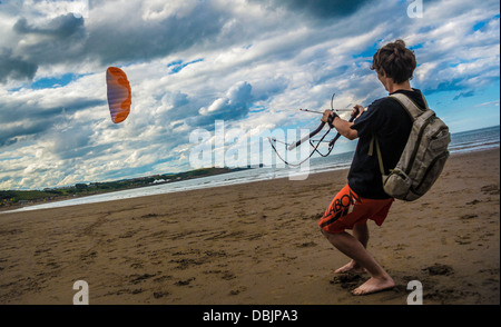 Jeune homme inidentifiable, adulte caucasien, volant d'un cerf-volant sur la plage de North Bay à Scarborough, dans le North Yorkshire, au Royaume-Uni. Banque D'Images