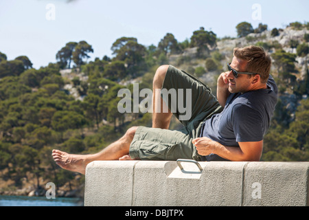 La Croatie, Dalmatie, jeune homme à bord de l'eau à l'aide de Phone Banque D'Images