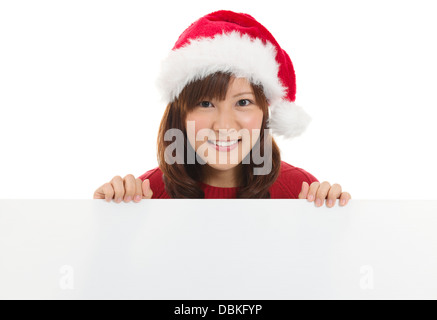 Santa Noël Cute Asian woman smiling and showing blank panneau vide. Chinois asiatique japonais / jeune modèle féminin en rouge Santa hat. Isolé sur fond blanc. Banque D'Images