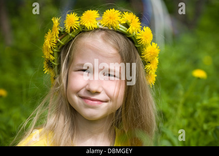 Closeup portrait of smiling little girl en couronne de pissenlit sur fond d'herbe verte Banque D'Images