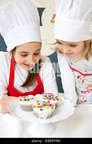 Petite fille avec chapeau de chef à la recherche à muffins, Munich, Bavière, Allemagne Banque D'Images