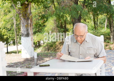 Les cadres supérieurs l'homme assis à la table et le menu de lecture dans un restaurant en plein air en été Banque D'Images