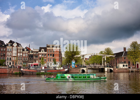 Vue sur la rivière d'Amsterdam, les maisons historiques, pont-levis et bateau à passagers en tournée, en Hollande, aux Pays-Bas. Banque D'Images