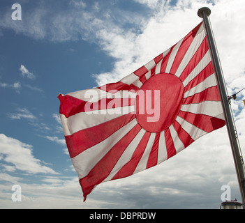 L'enseigne de la marine japonaise : le soleil levant, un drapeau blanc avec un disque rouge légèrement pour le palan avec 16 rayons de s'étendre. Banque D'Images
