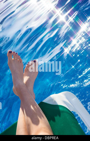 Une jeune femme se détend avec ses pieds sur un transat près de la piscine. Banque D'Images