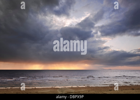 Se tenait sur le rivage à Ayr en regardant les nuages de tempête ensoleillée pendant l'île d'Arran à l'horizon. Banque D'Images