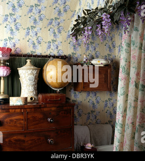 Globe Antique atlas et pot sur la poitrine en acajou-de-tiroirs en chalet avec salle de bains papier peint fleuri bleu et rose rideaux Banque D'Images