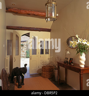 Bouquet de lys blancs sur table console en pays hall avec à côté de l'éléphant en bois demi-ouverte Porte avant vitrée Banque D'Images