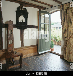 Tall-retour chaise en bois fabriqués à la main et le plancher en brique gris hall cottage avec rideau épais à côté de porte avant Banque D'Images